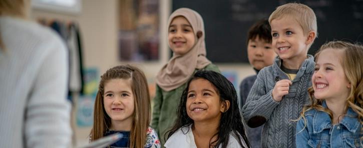 kids sitting amd smiling with attention to someone holding a book