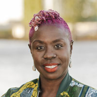 a Black woman with short pink hair and orange lipstick sitting outside