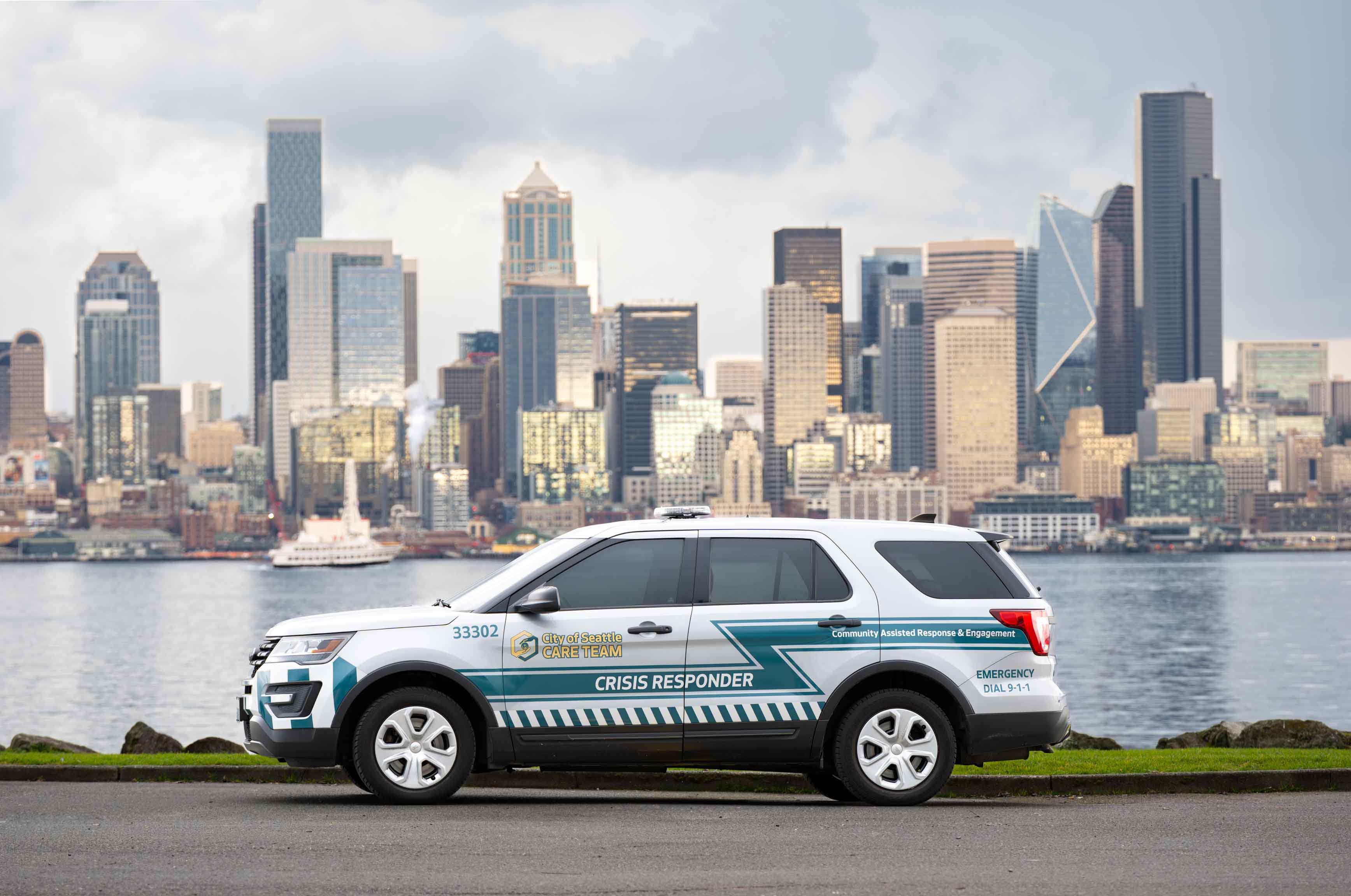 Image shows CARE crisis responder vehicle with city of Seattle cityscape in background, behind water from Puget Sound. 