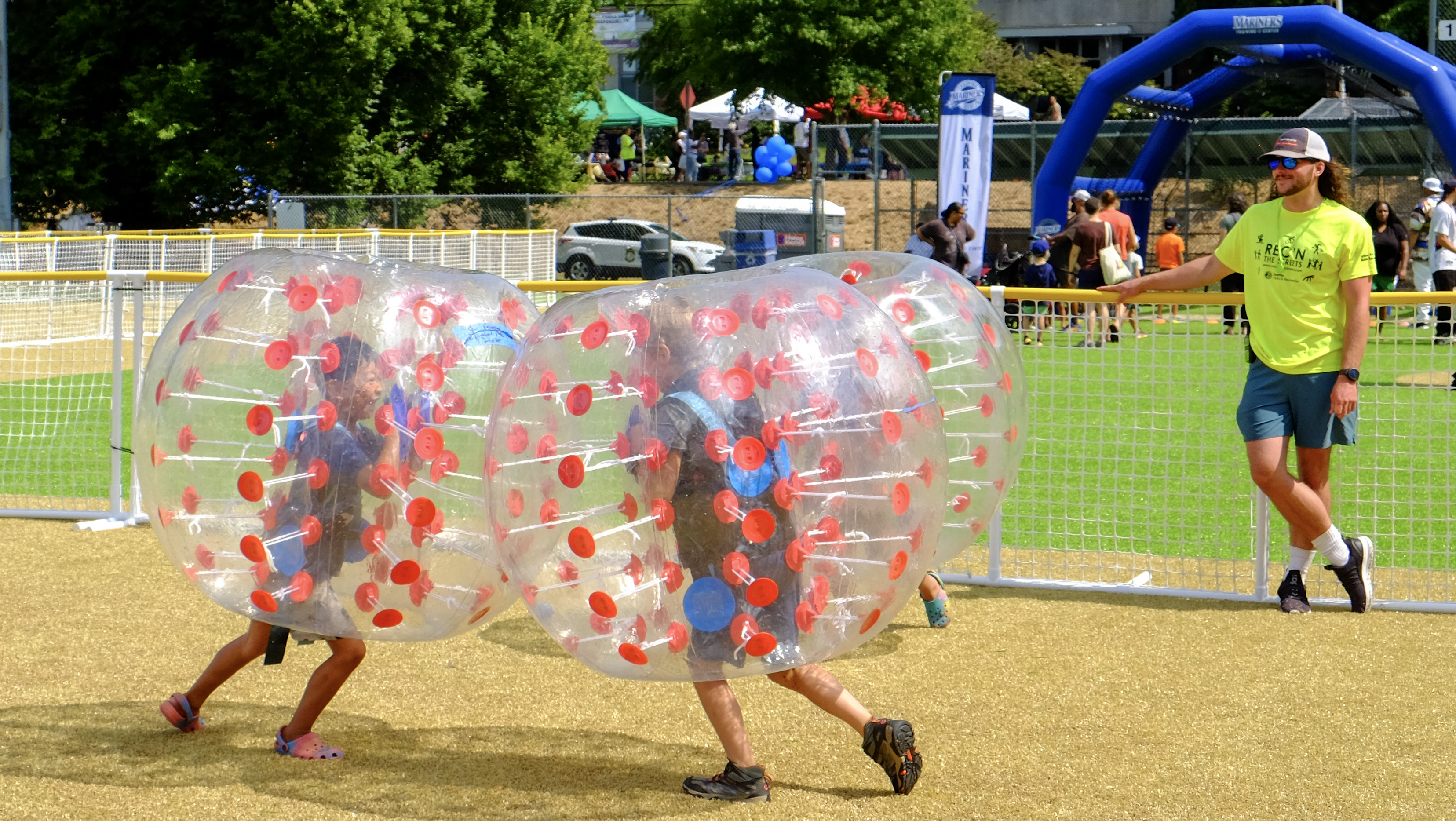 2 children play inside inflatable balls while an adult watches