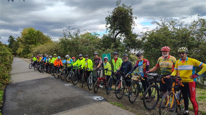 Group of cyclists on the newly completed Burke-Gilman Trail improvements, wearing bright gear and helmets, posing with their bikes
