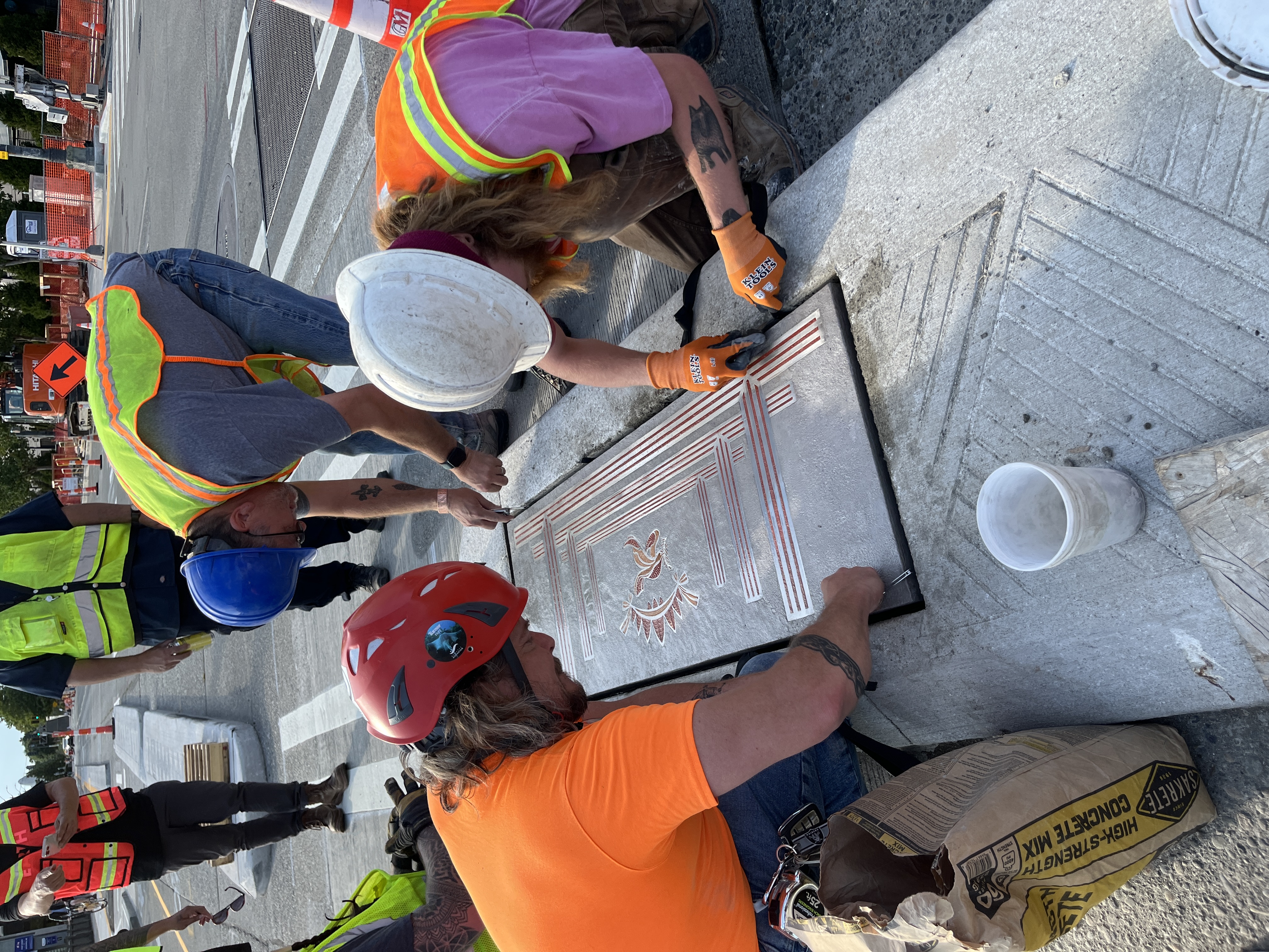 Crews installing steel inlay art in new bike buffer between Vine St and Wall St.