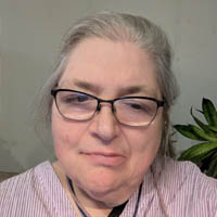 Dorene Cornwell has glasses, a pink shirt, and gray hair