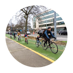 A man on a bike on a protected bike lane, with a group of children behind him, also on bikes