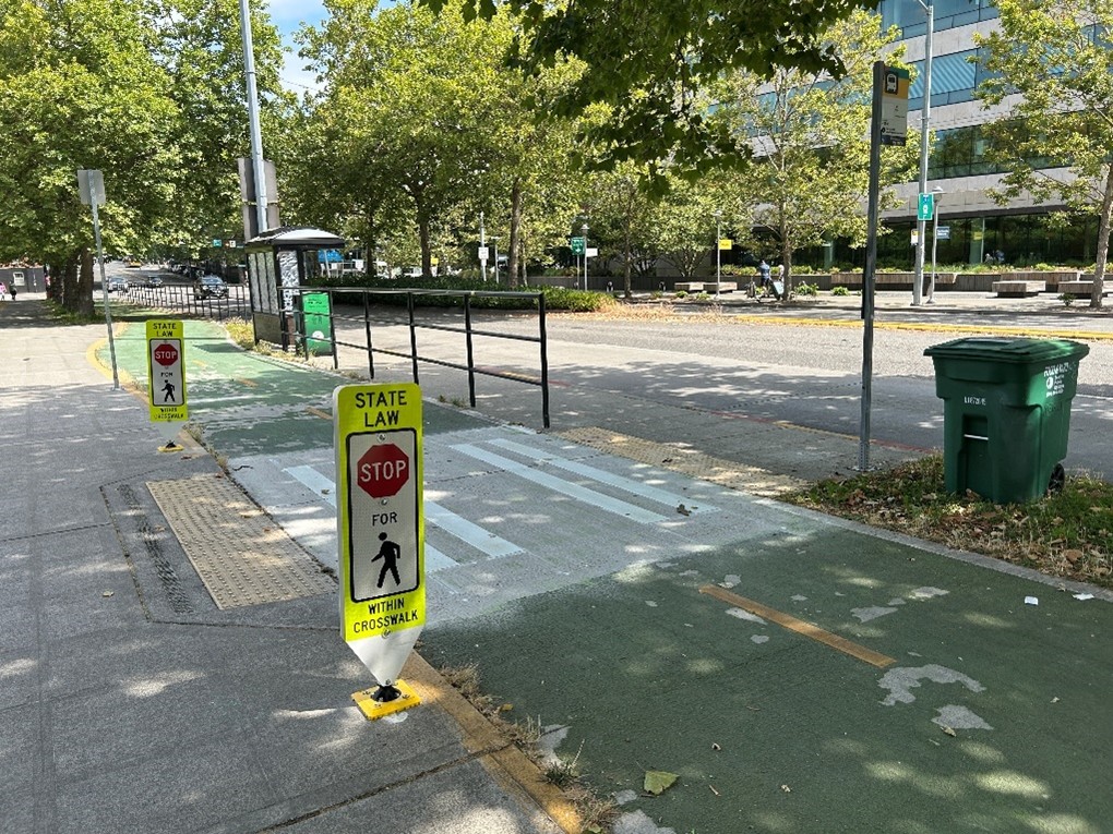 A crosswalk with parking crossing signs going over a bicycle lane to a transit island.