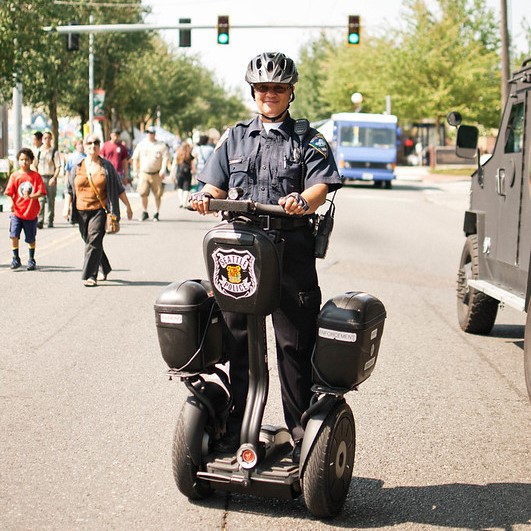 A uniformed Seattle police officer smiles at the camera while riding a Segway at a community parade