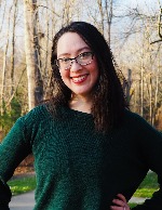 Rose smiling broadly at the camera in a green sweater with trees in the background.
