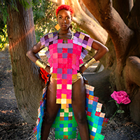 Model Acacia wearing a garment composed of multicolored square matboards.