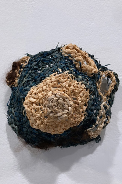 Circular Woven piece with teal and beige fiber.