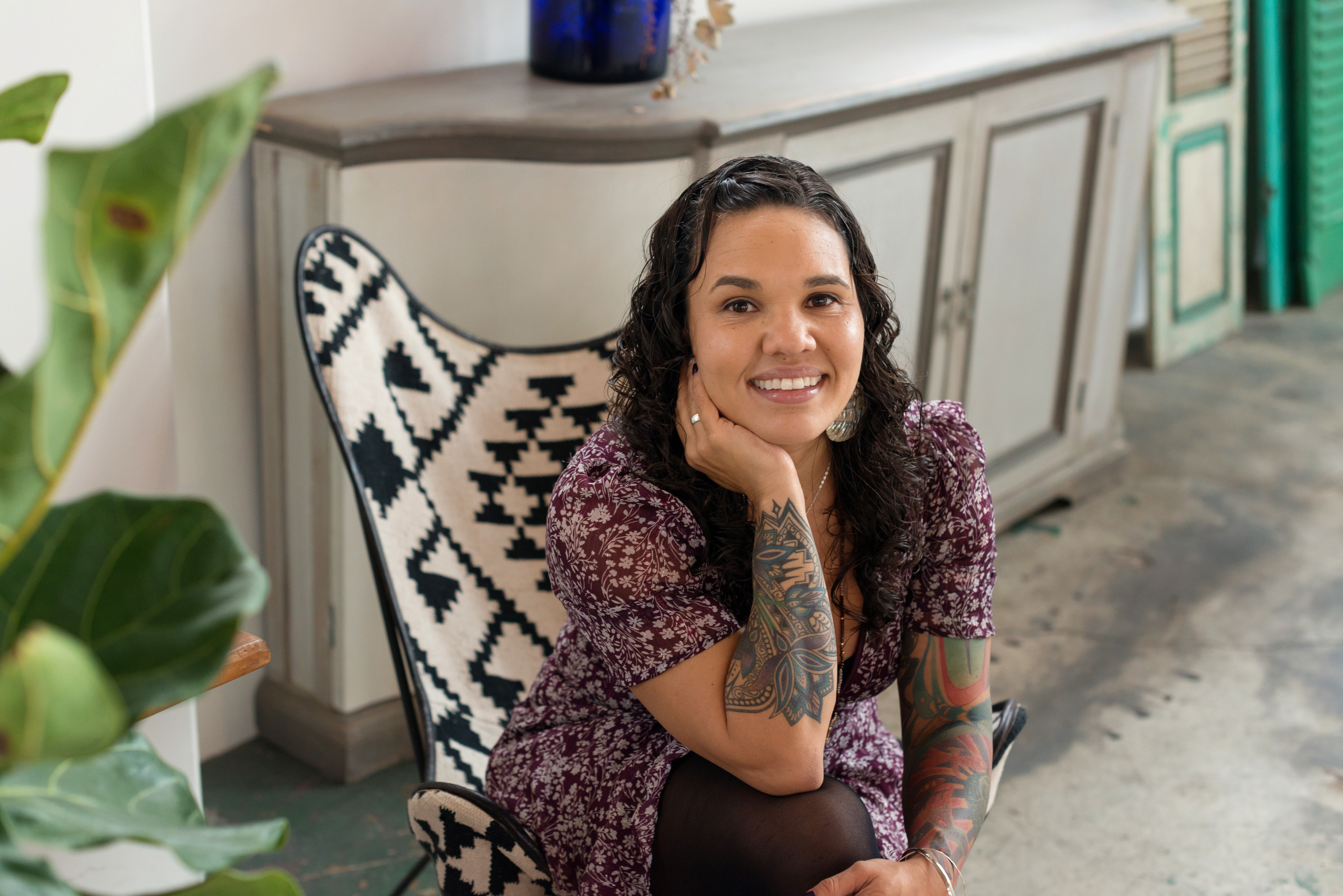 Photo of Rachel Heaton sitting indoors smiling in a dress.  