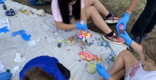 3 children painting on a drop cloth in a park
