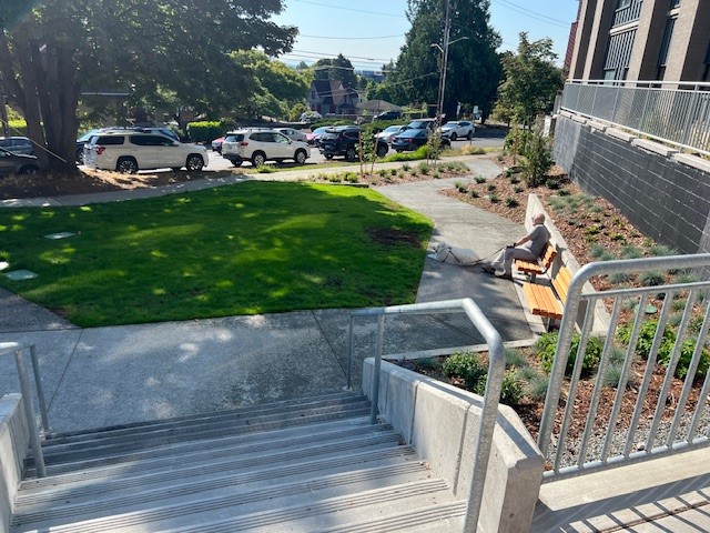 Stairs leading to park lawn with a bench, pathways, and garden beds