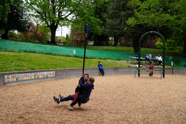 Two children ride together on a zip line at a playground 