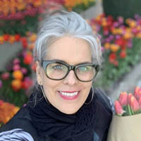 Photo of Lisa Harrison, smiling outside by a flowers. 