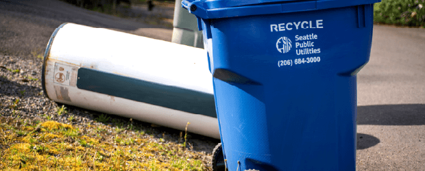 A water heater beside a recycling bin.