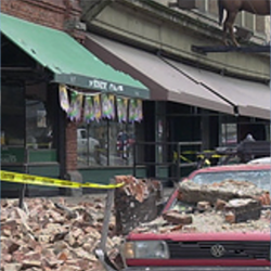 A car on the side of street with debris on top of it due to an earthquake